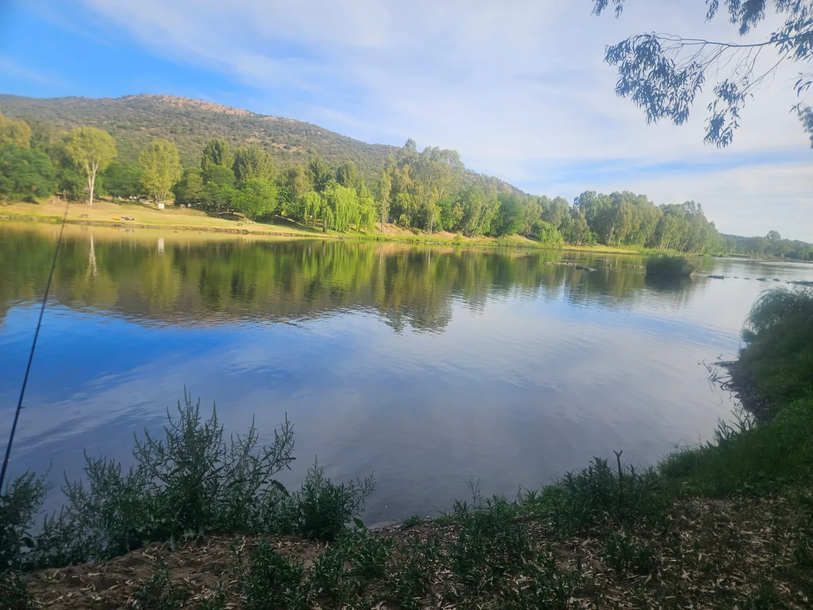 The wide, calm river at Destination Unknown with tree-covered hills reflected in the water