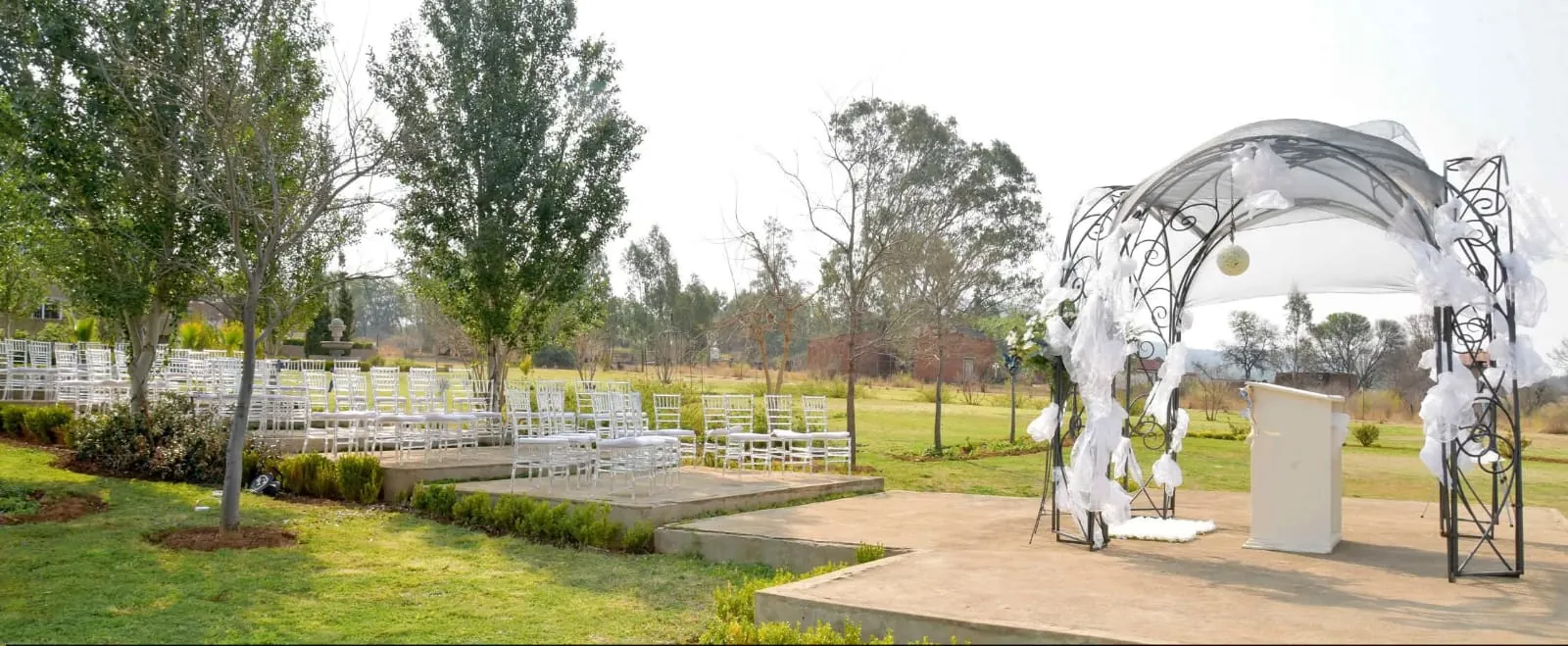 Garden ceremony set-up with a white arch and chairs on the lawn