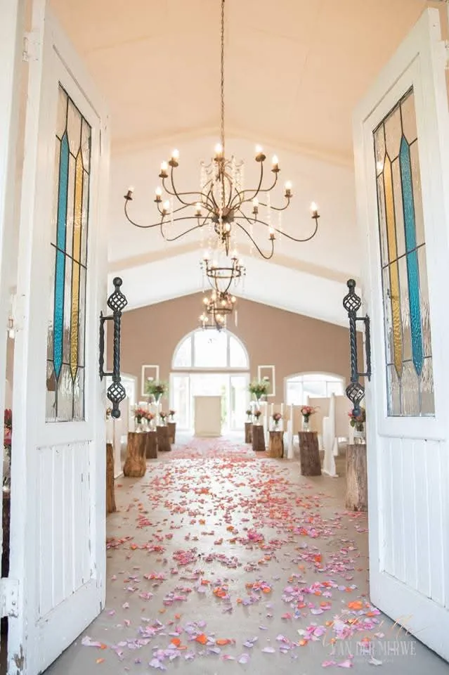 Aisle with rose petals leading through white doors under a chandelier